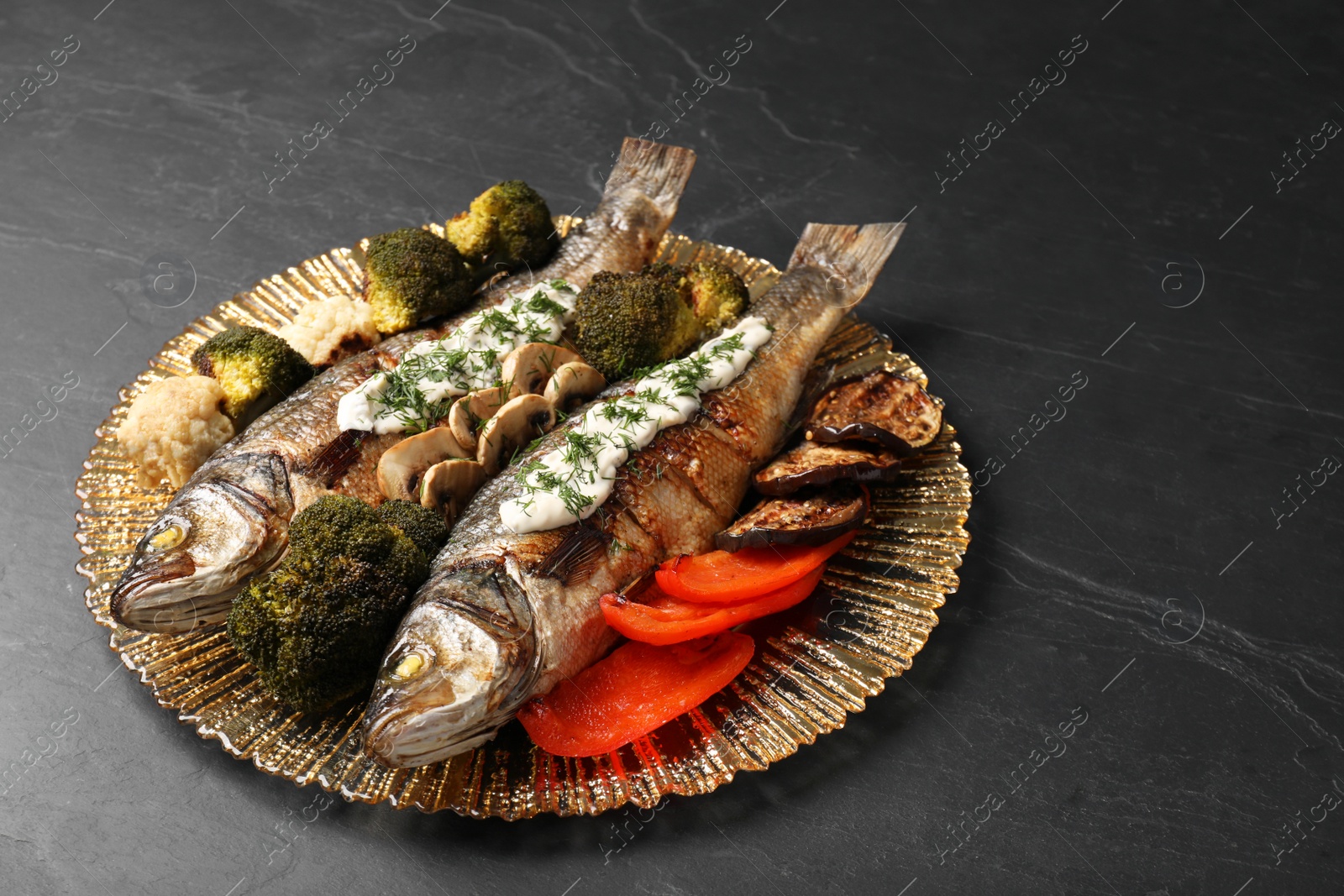 Photo of Plate with delicious baked sea bass fish and sauce on black table