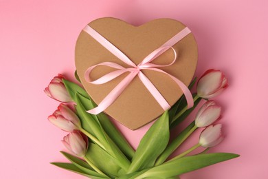Photo of Heart shaped gift box with bow and beautiful tulips on pale pink background, flat lay