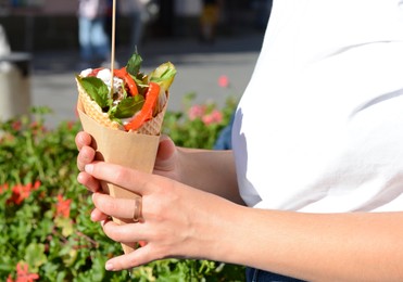 Photo of Woman holding wafer with falafel and vegetables outdoors, closeup. Street food