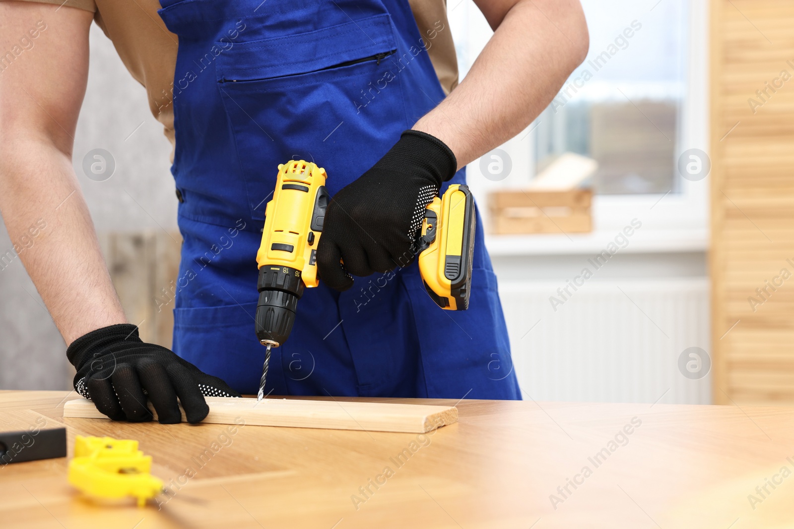 Photo of Young worker using electric drill at table in workshop, closeup