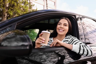 Photo of Young woman with cup of coffee sitting inside her modern car