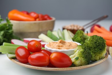 Plate with delicious hummus and fresh vegetables on white table, closeup