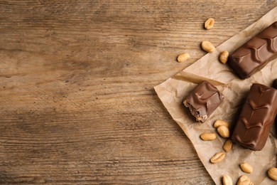 Photo of Chocolate bars with nuts and parchment on wooden table, flat lay. Space for text