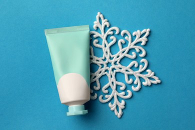 Photo of Tube of hand cream and snowflake on light blue background, flat lay. Winter skin care