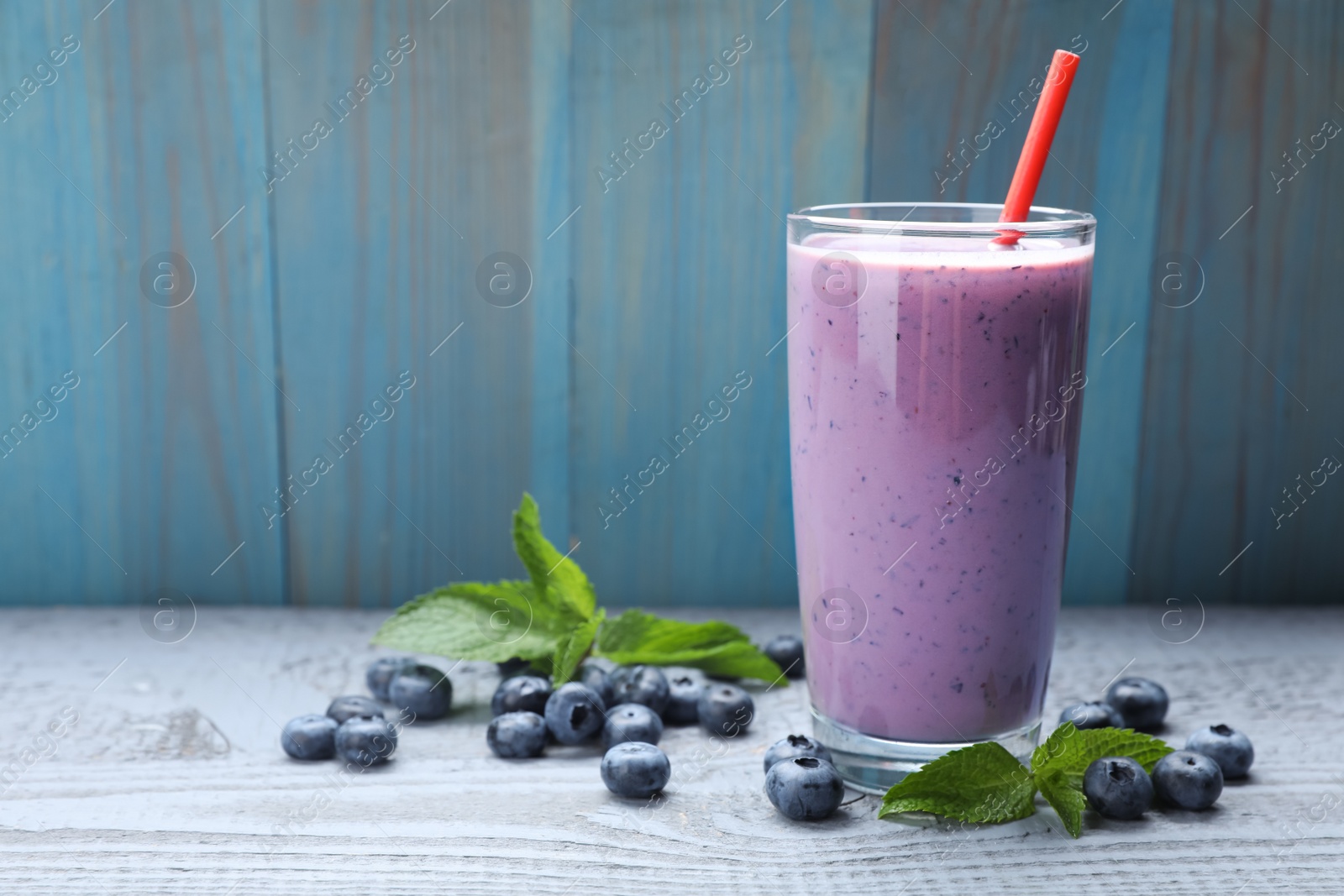 Photo of Glass of freshly made blueberry smoothie on grey wooden table. Space for text