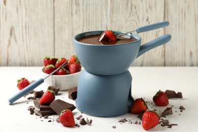 Fondue pot with chocolate and fresh strawberries on white table