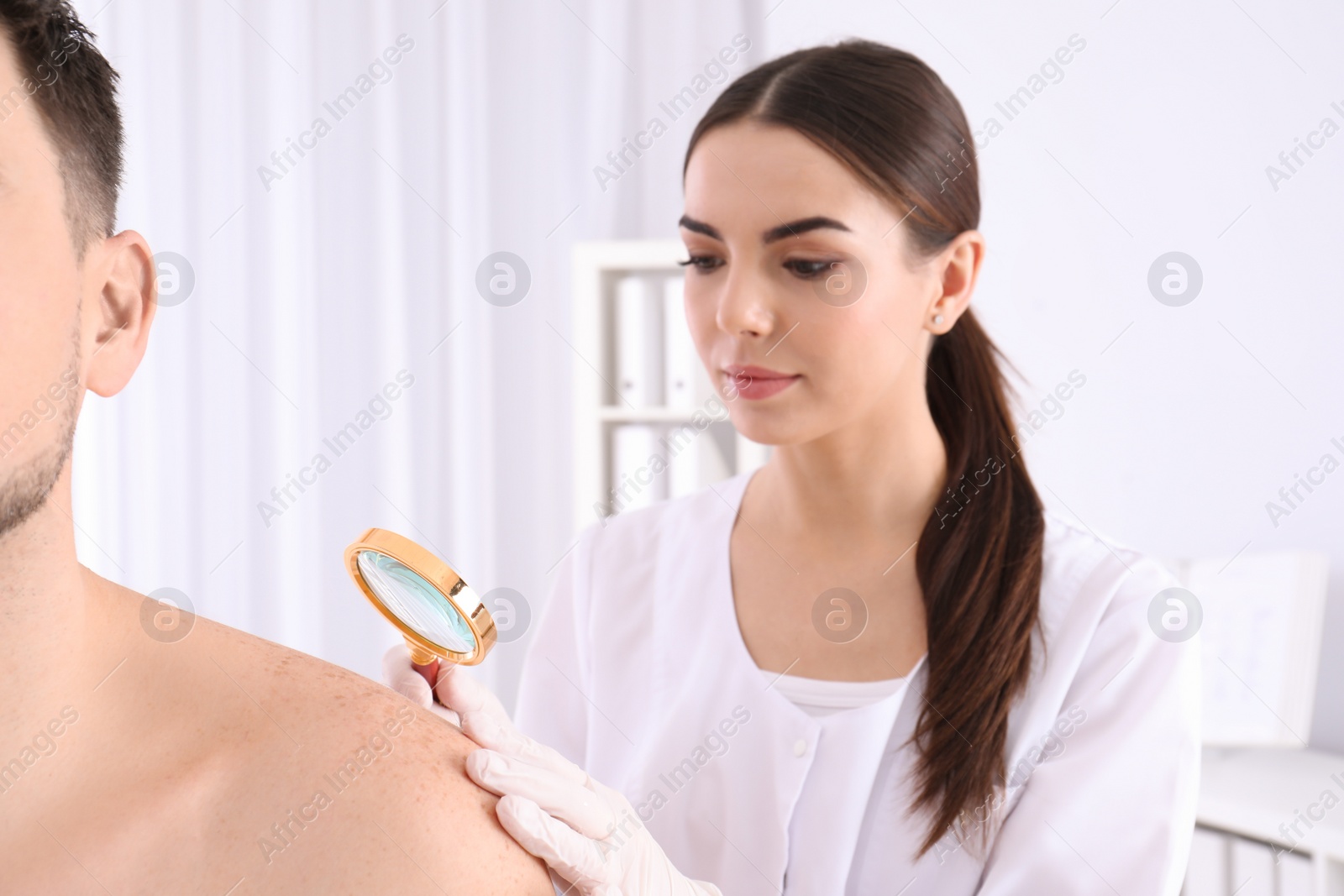 Photo of Dermatologist examining patient with magnifying glass in clinic