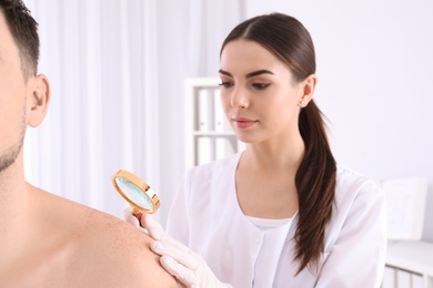 Dermatologist examining patient with magnifying glass in clinic