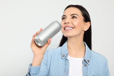 Beautiful happy woman holding beverage can on light grey background, closeup