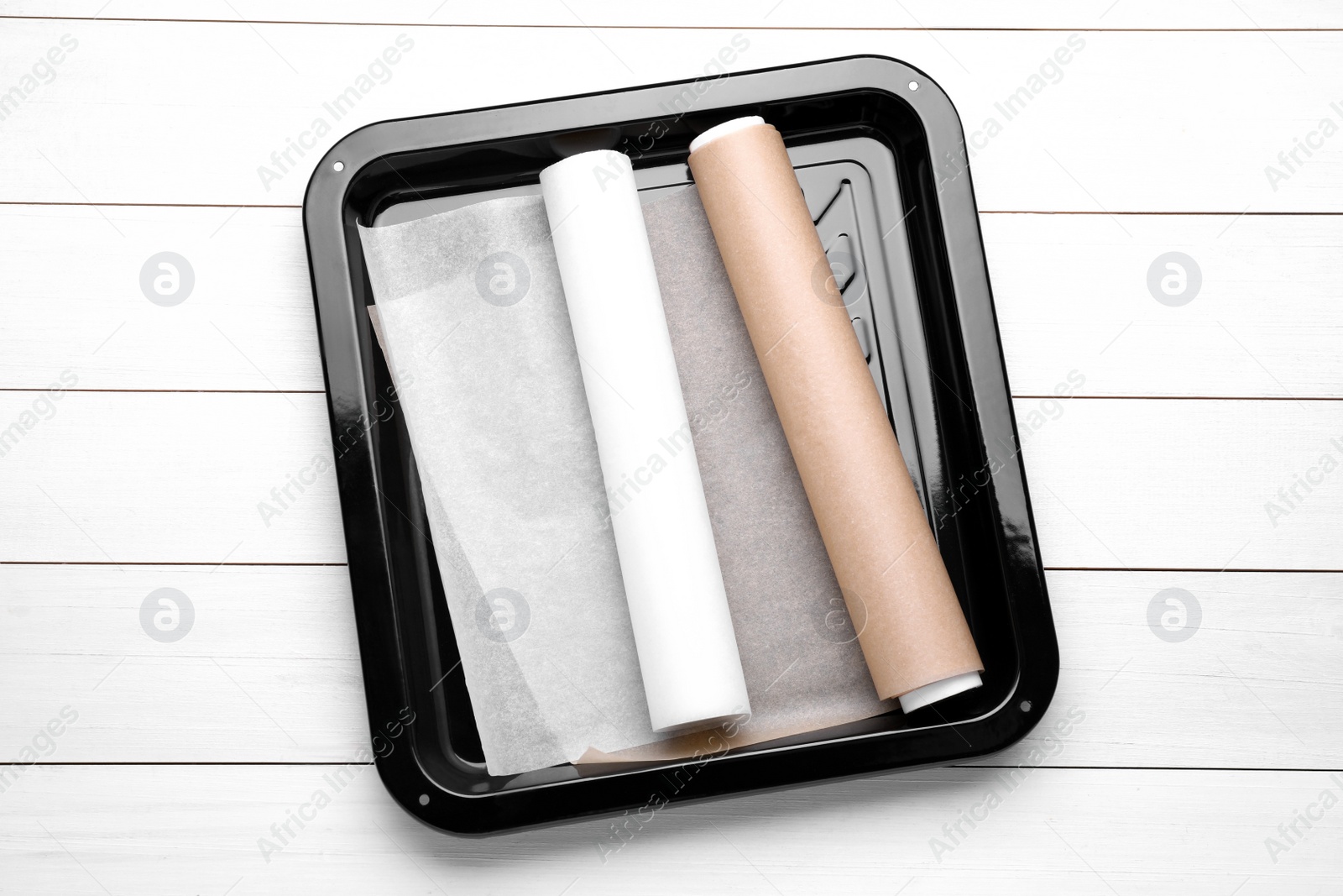 Photo of Rolls of parchment paper in baking pan on white wooden table, top view