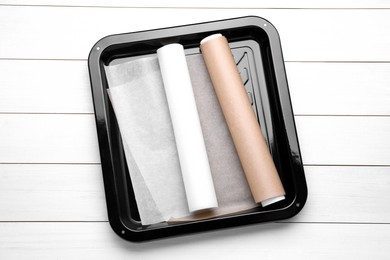 Rolls of parchment paper in baking pan on white wooden table, top view