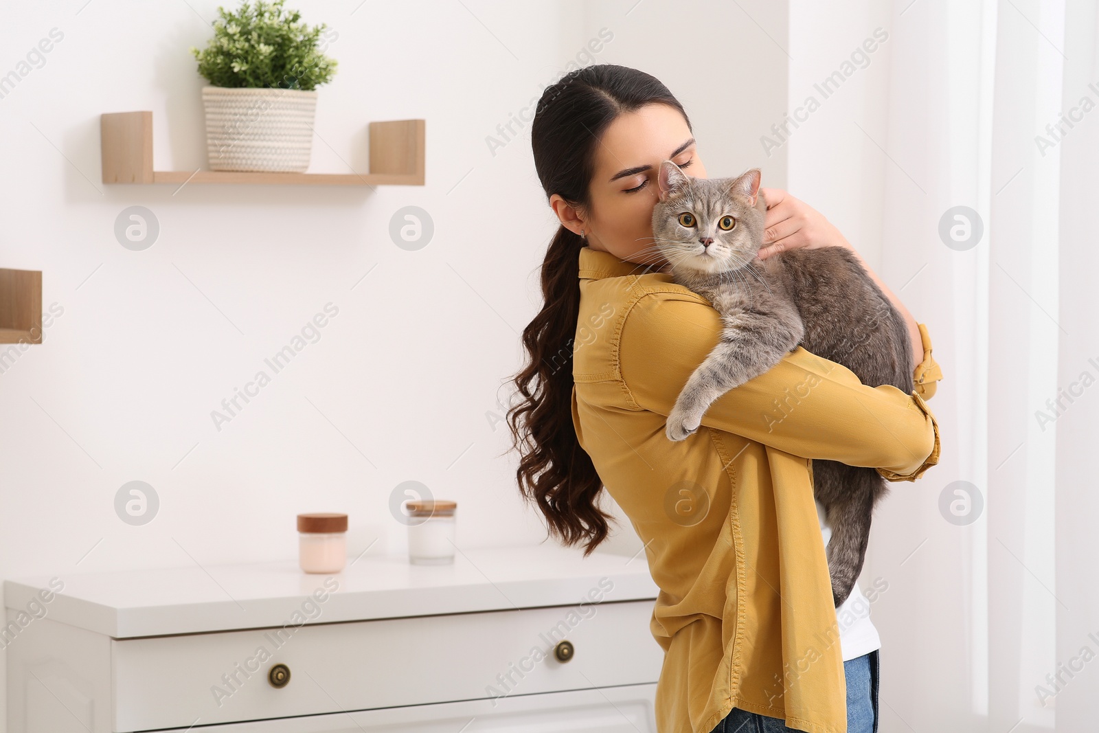 Photo of Young woman kissing her adorable cat at home, space for text