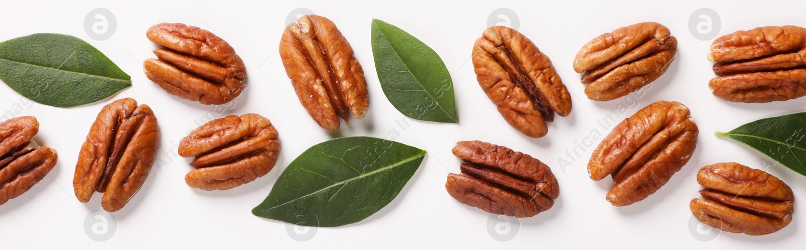 Photo of Delicious pecan nuts and green leaves on white background, flat lay