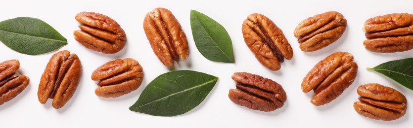 Delicious pecan nuts and green leaves on white background, flat lay