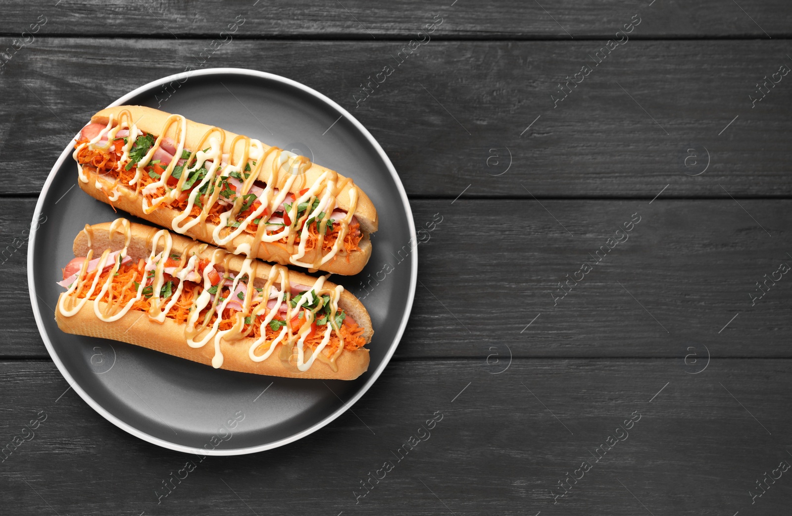 Photo of Delicious hot dogs with bacon, carrot and parsley on black wooden table, top view. Space for text