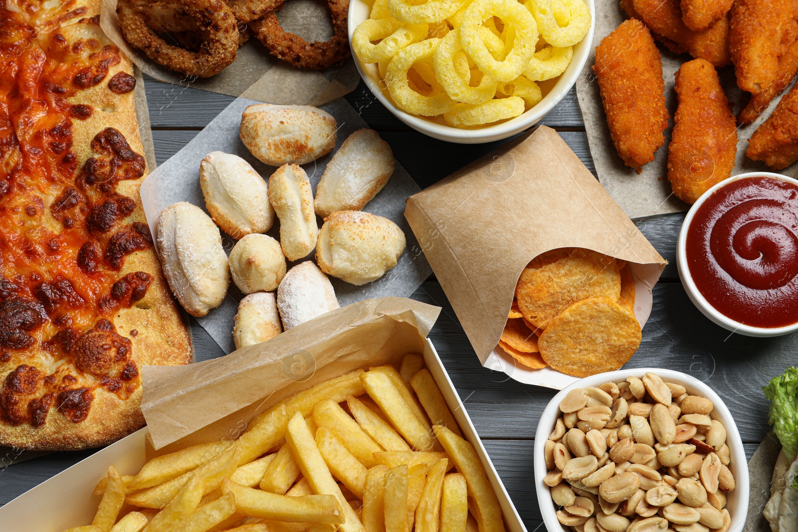 Photo of French fries, chips other fast food on gray wooden table, flat lay