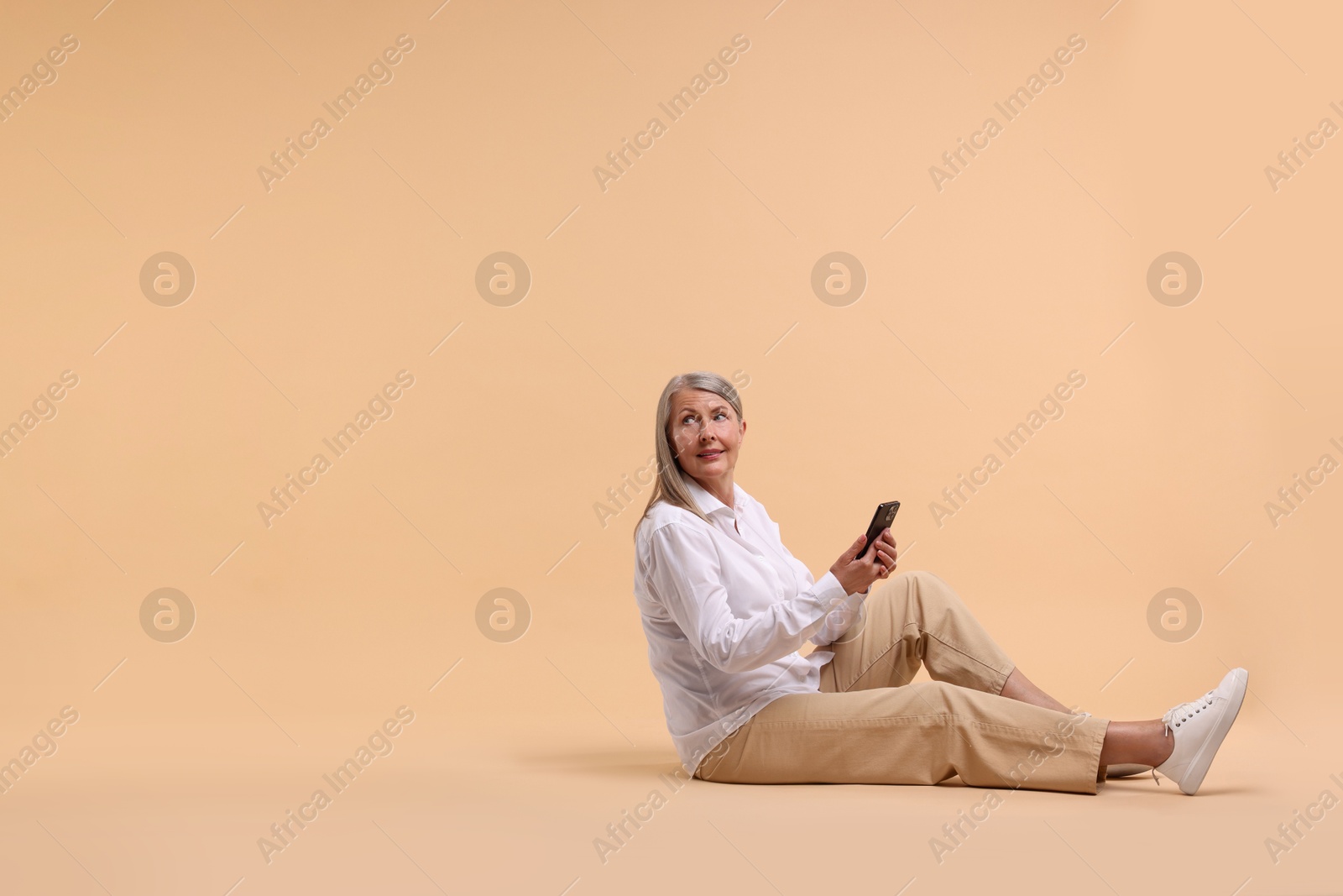 Photo of Senior woman with phone on beige background, space for text