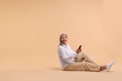 Photo of Senior woman with phone on beige background, space for text