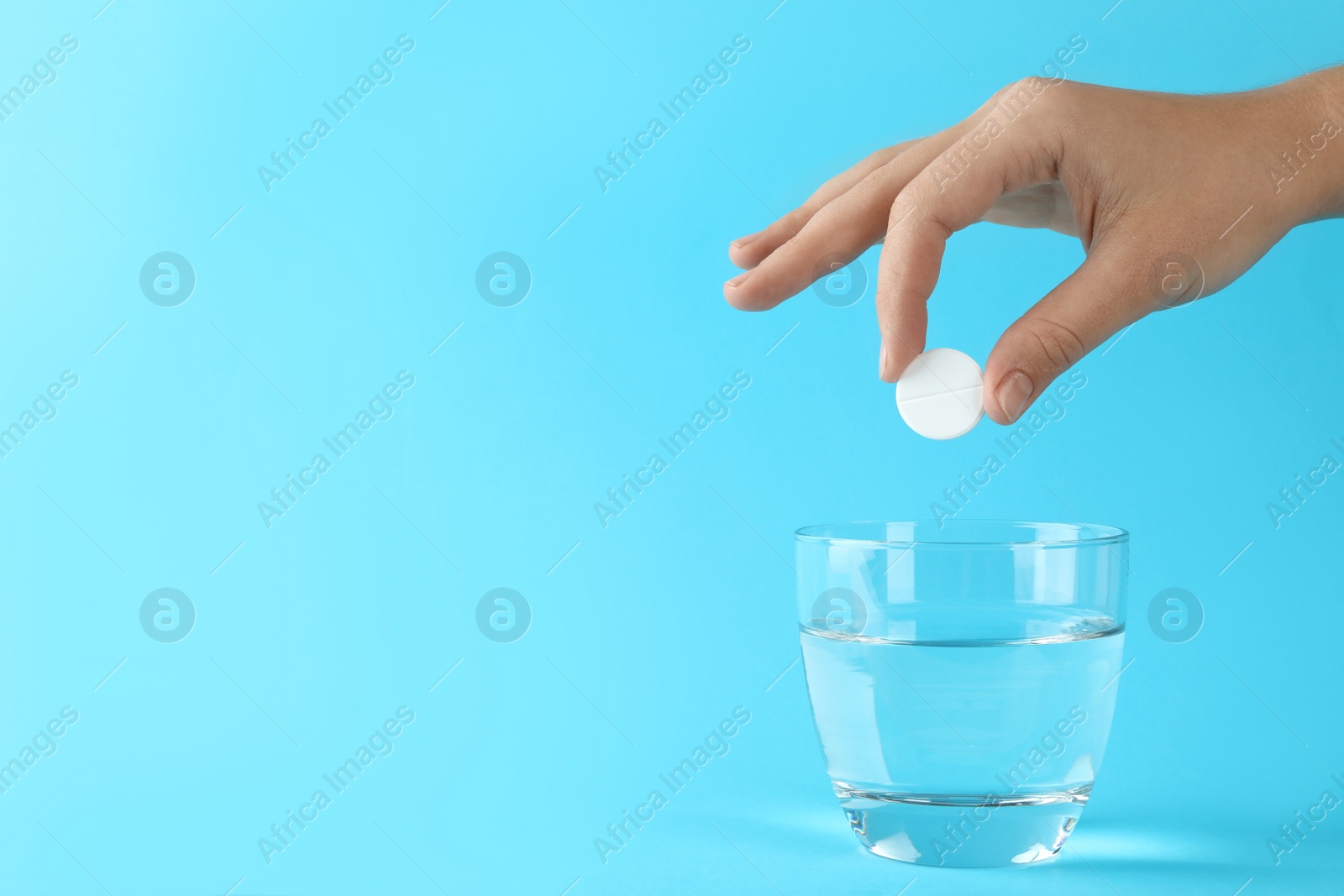 Photo of Woman putting tablet into glass of water on light blue background, space for text