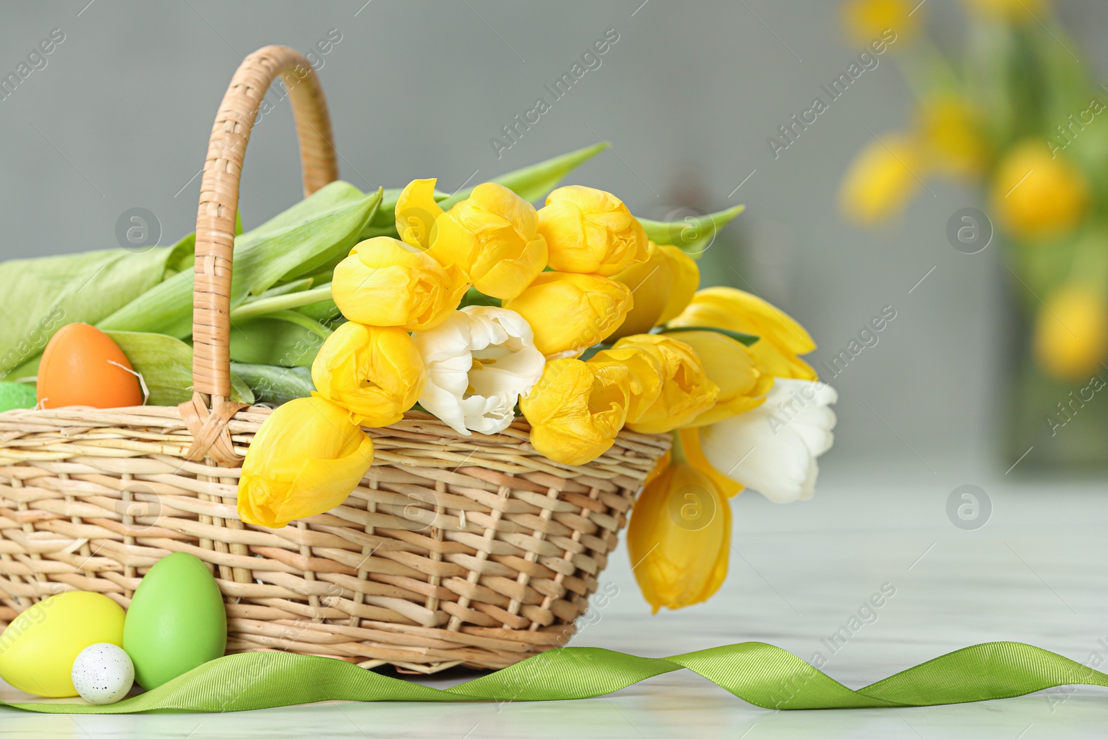 Photo of Easter basket with bouquet of tulips and eggs on white marble table indoors, closeup