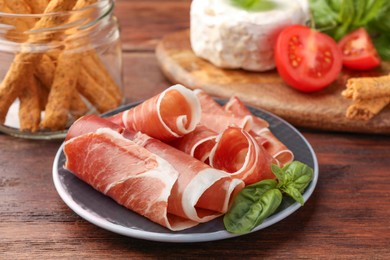 Photo of Rolled slices of delicious jamon and basil on wooden table, closeup