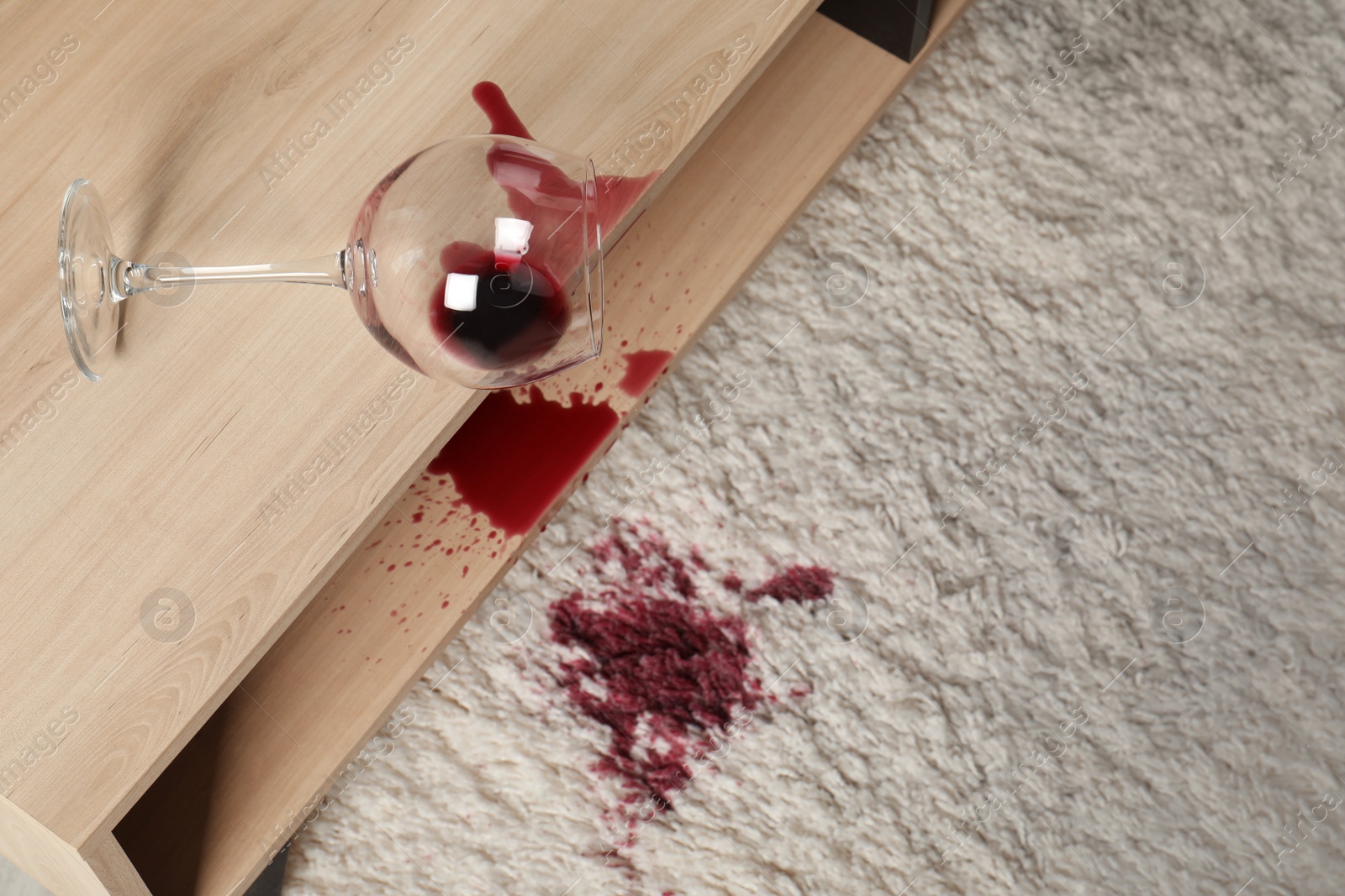 Photo of Overturned glass and spilled red wine on white carpet indoors, above view