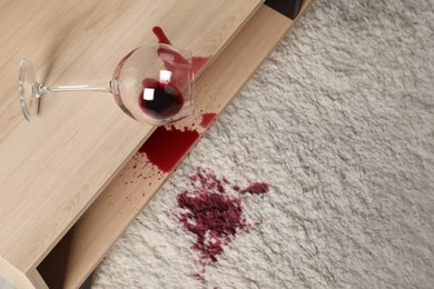 Photo of Overturned glass and spilled red wine on white carpet indoors, above view