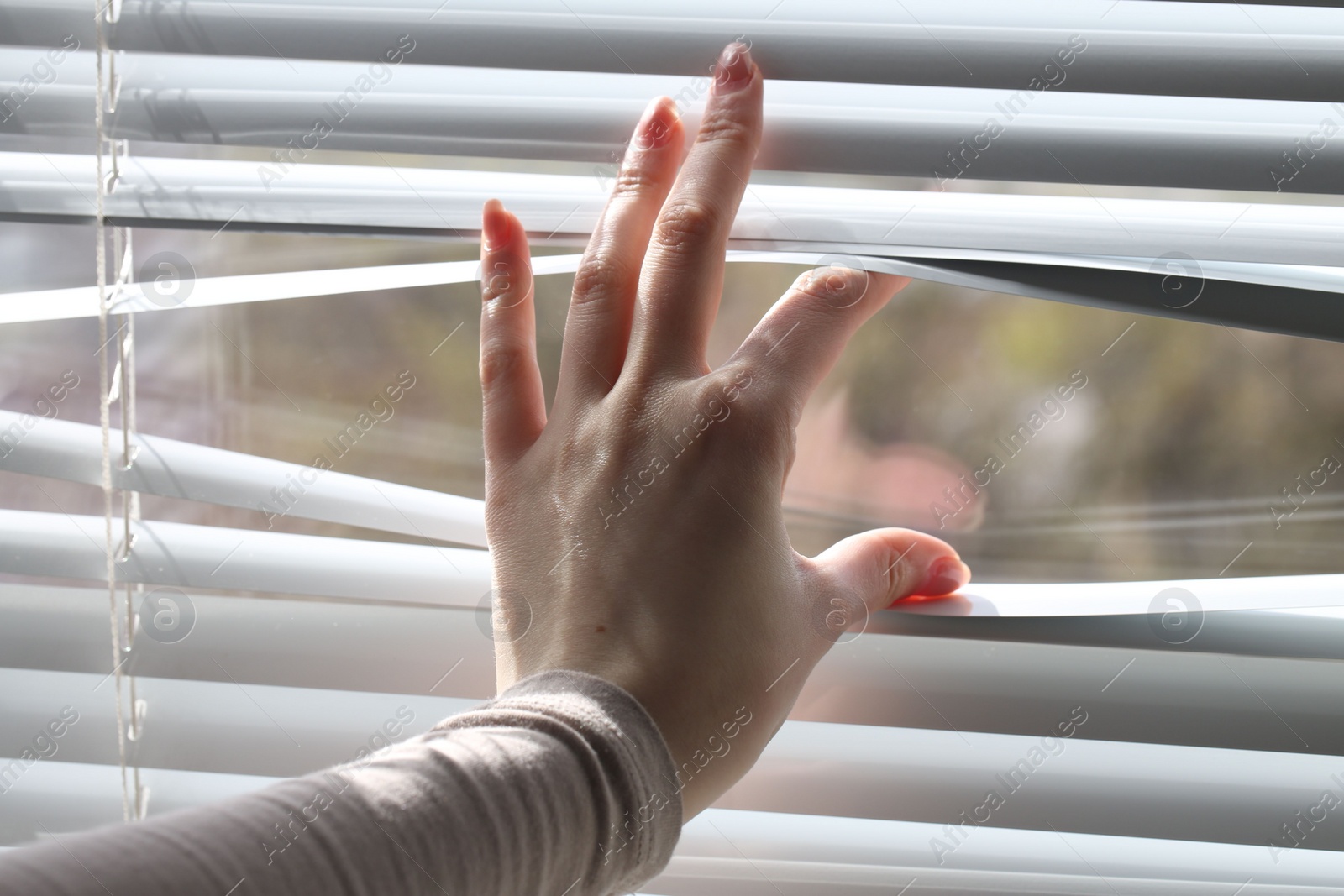 Photo of Woman separating slats of white blinds indoors, closeup