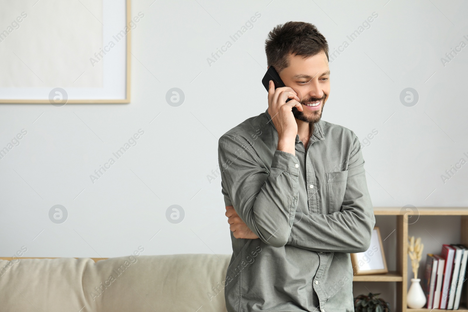 Photo of Happy man talking on smartphone at home, space for text