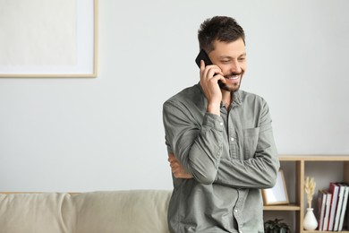 Happy man talking on smartphone at home, space for text