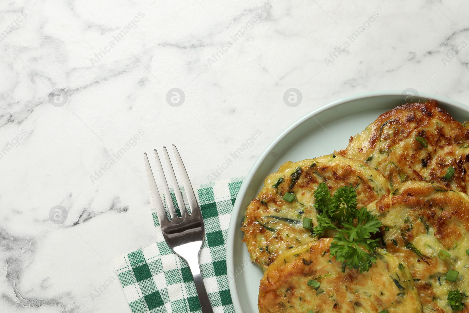 Photo of Delicious zucchini fritters served on white marble table, flat lay. Space for text