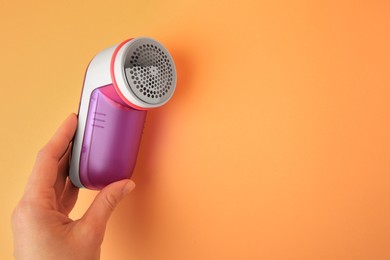 Photo of Woman holding modern fabric shaver on pale orange background, closeup. Space for text