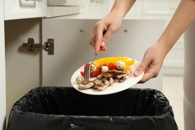 Woman throwing vegetable and mushrooms into bin indoors, closeup