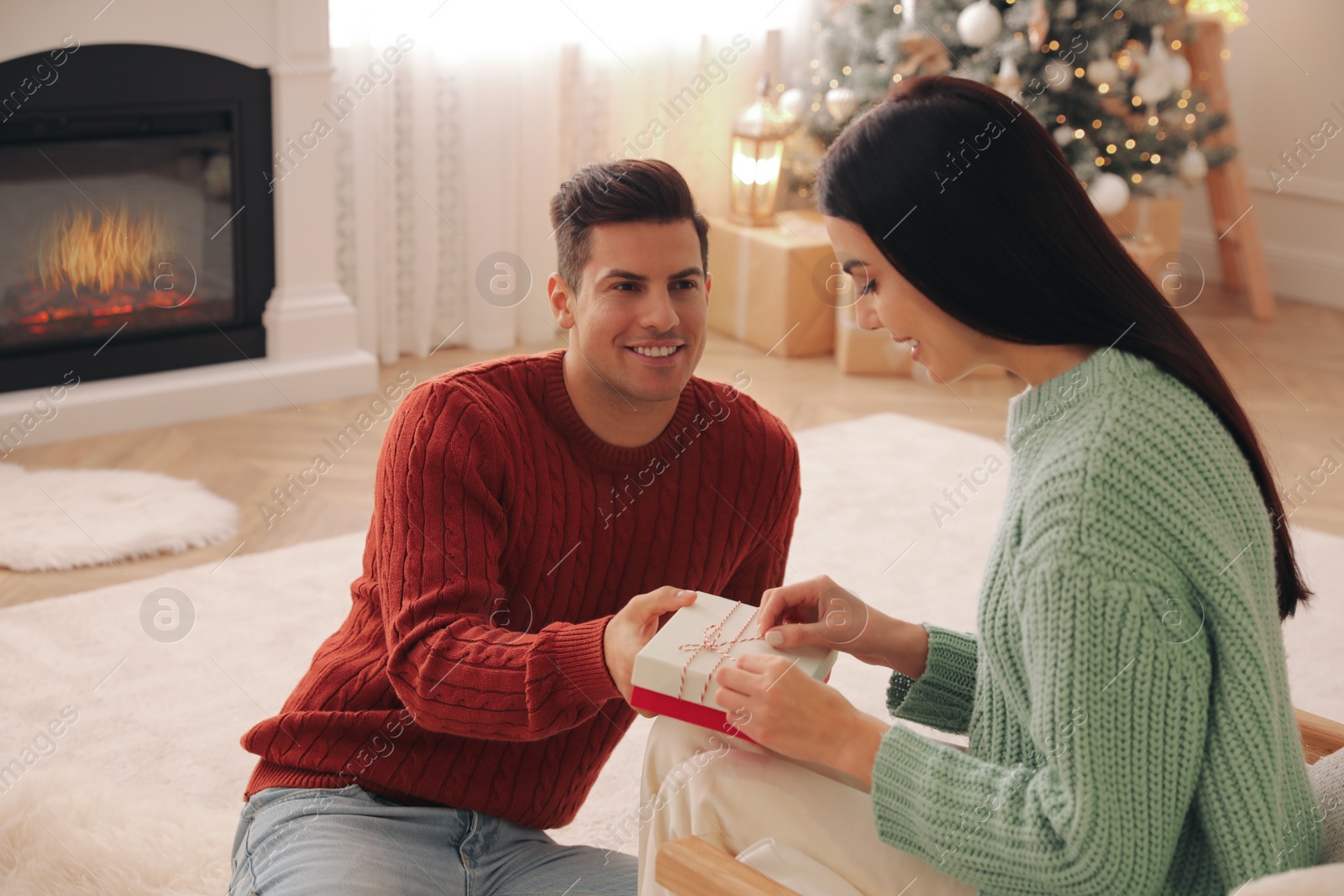 Photo of Boyfriend giving Christmas gift box to his girlfriend in living room