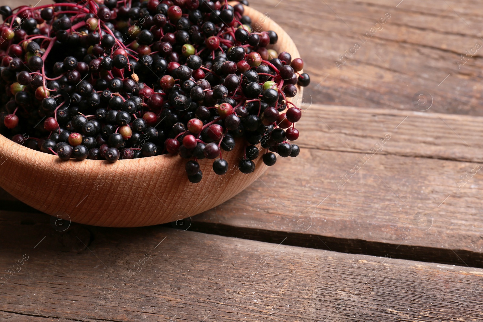 Photo of Bowl with tasty elderberries (Sambucus) on wooden table, closeup. Space for text