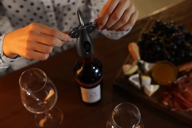Photo of Romantic dinner. Woman opening wine bottle with corkscrew at table indoors, above view