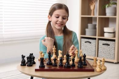 Photo of Cute girl playing chess at table in room