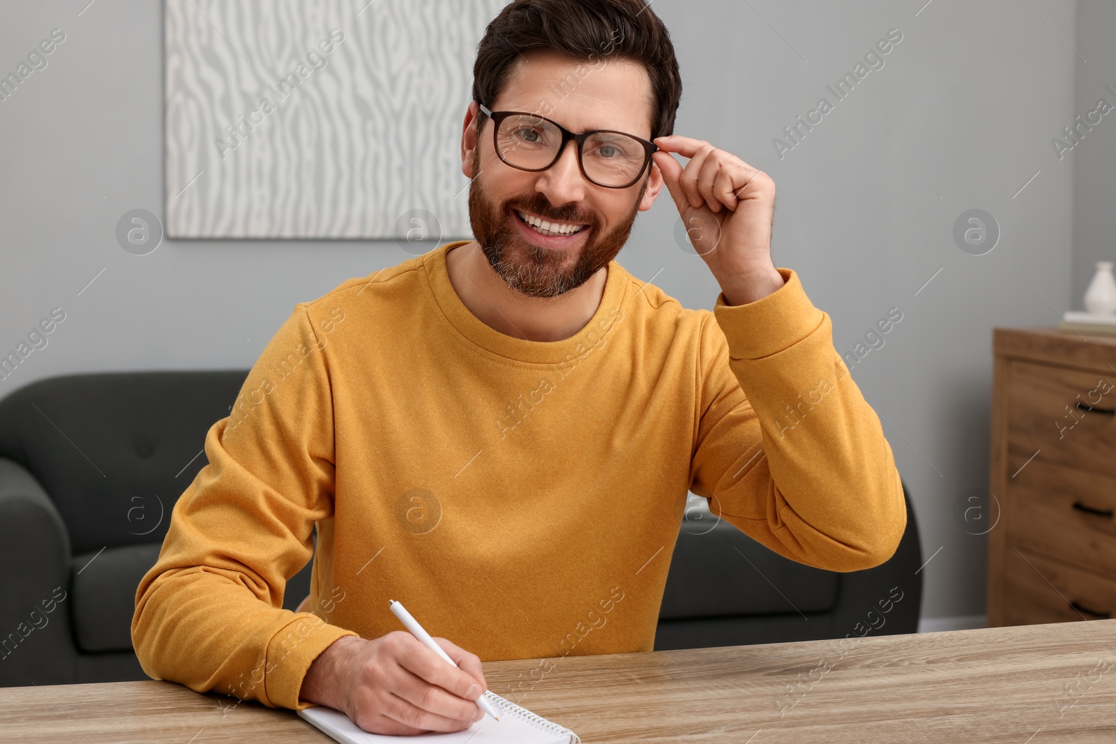 Photo of Man writing something into notebook at wooden table indoors
