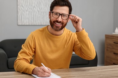 Man writing something into notebook at wooden table indoors