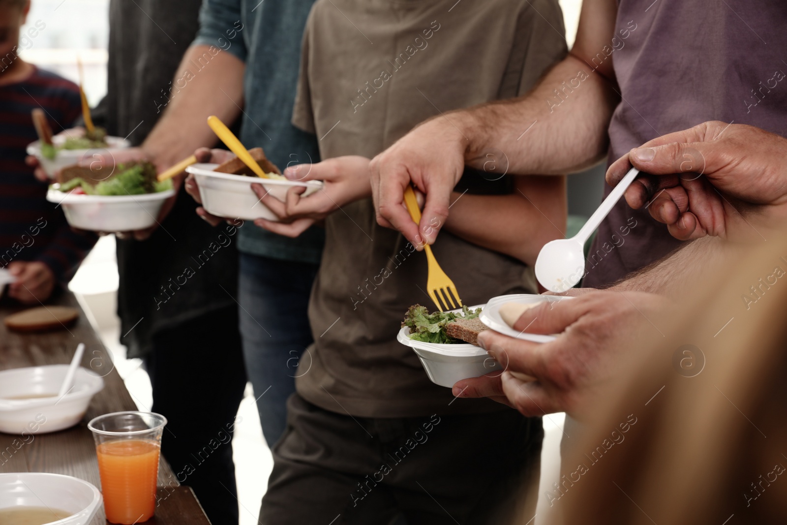 Photo of Poor people holding plates with food in charity centre, closeup