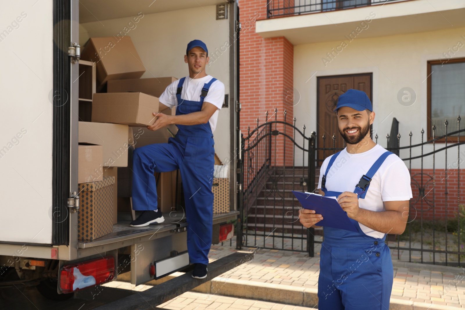 Photo of Moving service workers outdoors, unloading boxes and checking list