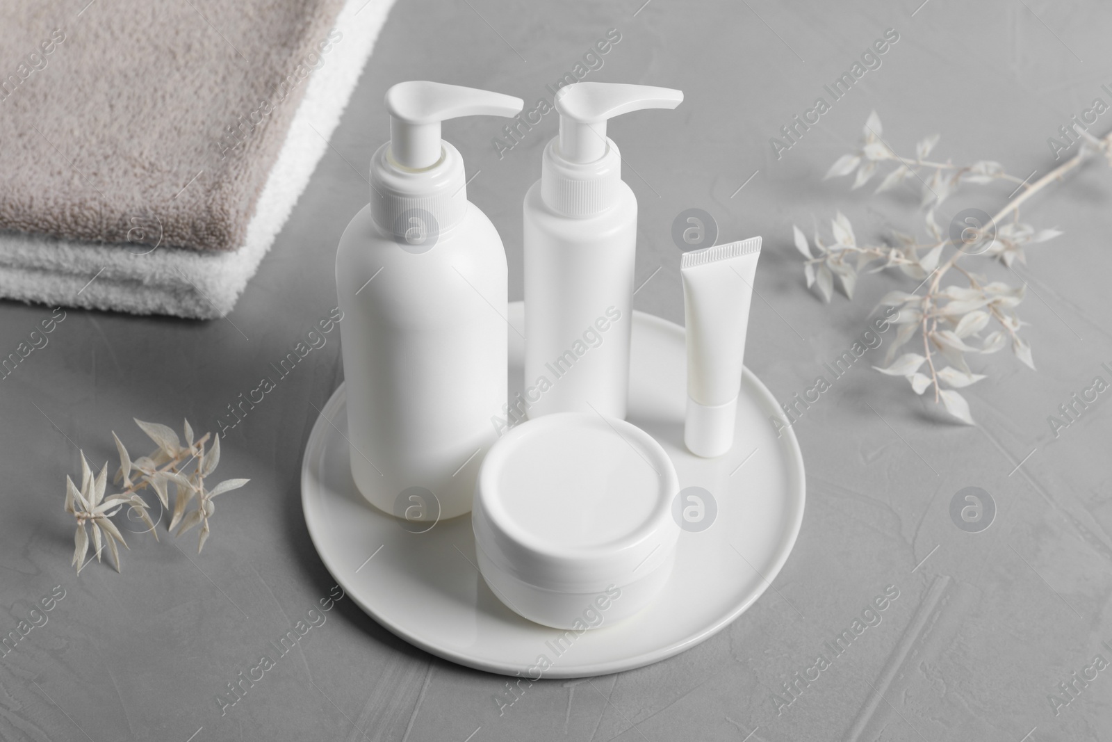 Photo of Different cosmetic products, towels and dry leaves on grey table