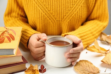 Photo of Woman with cup of hot drink at white wooden table, closeup. Cozy autumn atmosphere