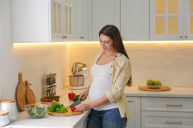 Young pregnant woman preparing vegetable salad at table in kitchen. Healthy eating