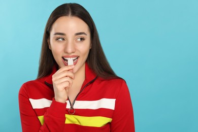 Photo of Woman putting bubble gum into mouth on light blue background. Space for text