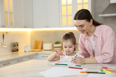 Mother and her little daughter drawing with colorful markers at table in kitchen. Space for text