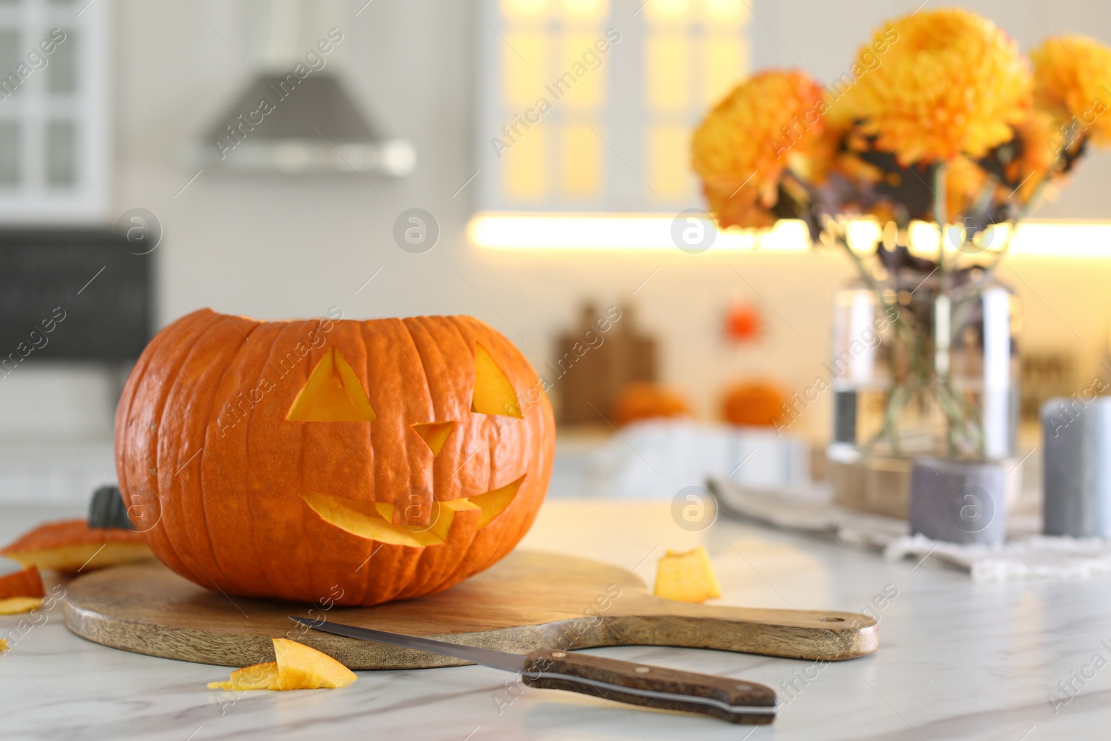 Photo of Pumpkin jack o'lantern on white marble table in kitchen, space for text. Halloween celebration