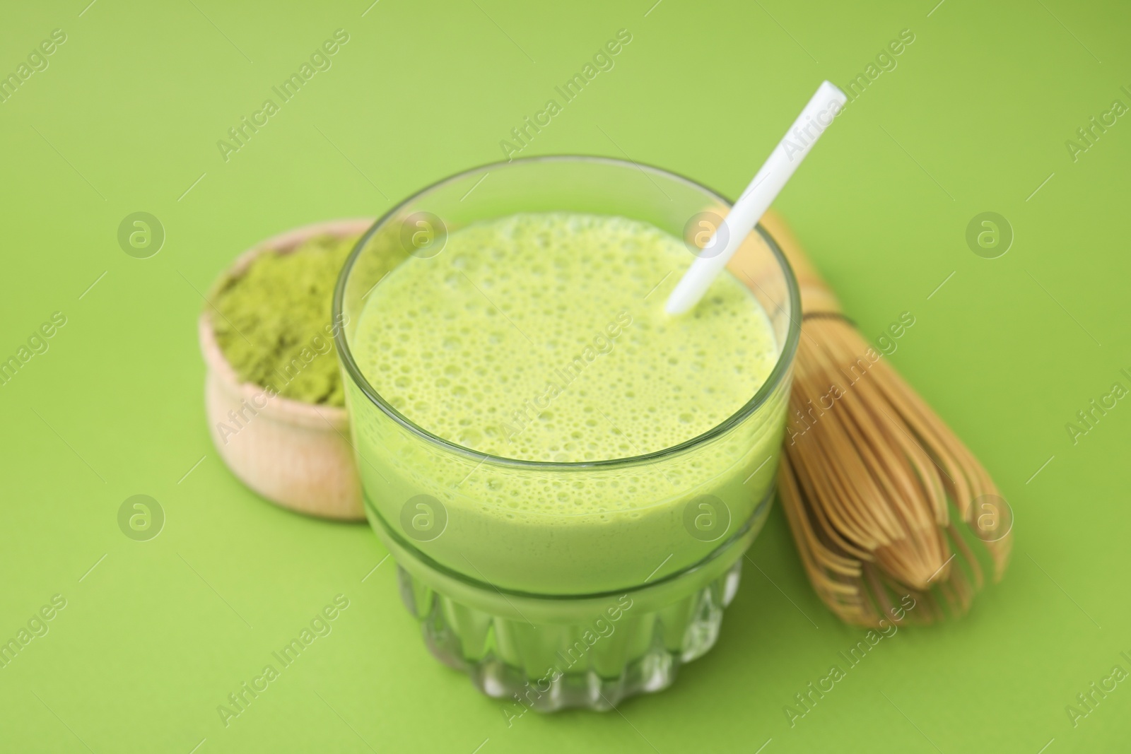 Photo of Glass of tasty matcha smoothie, powder and bamboo whisk on green background, closeup