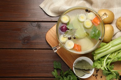 Photo of Glass pot with tasty bouillon and different ingredients on wooden table, flat lay. Space for text
