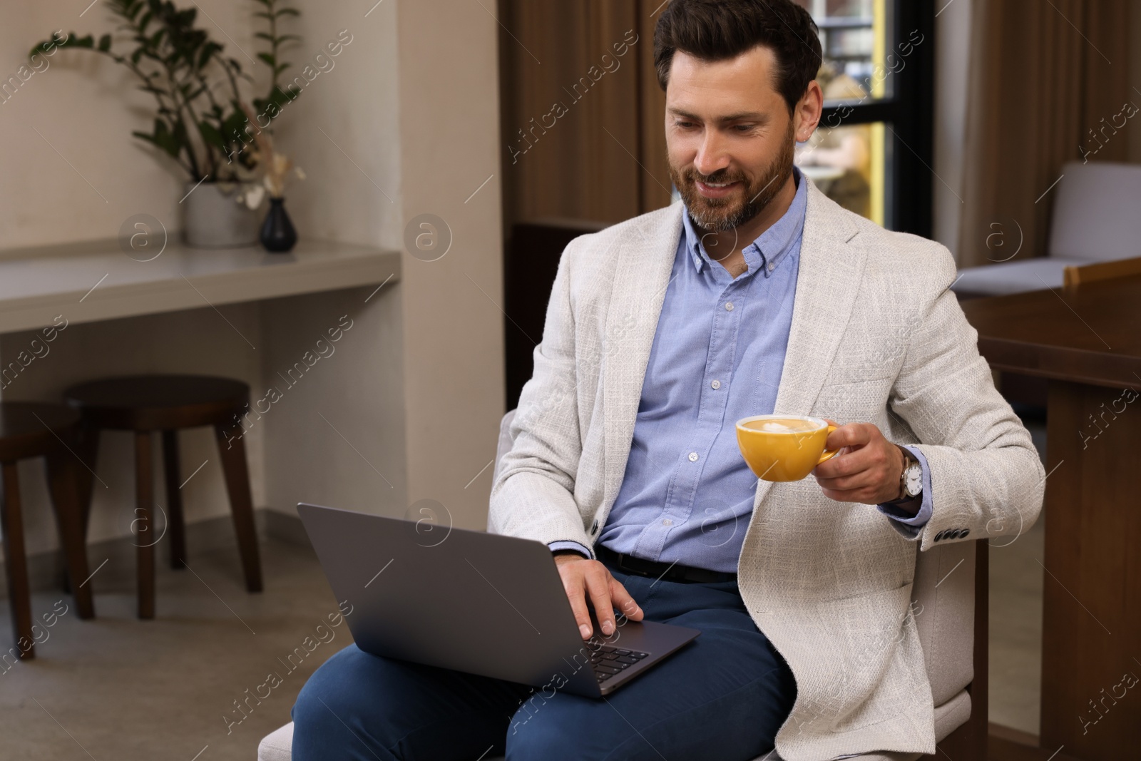 Photo of Man with cup of coffee using laptop in cafe